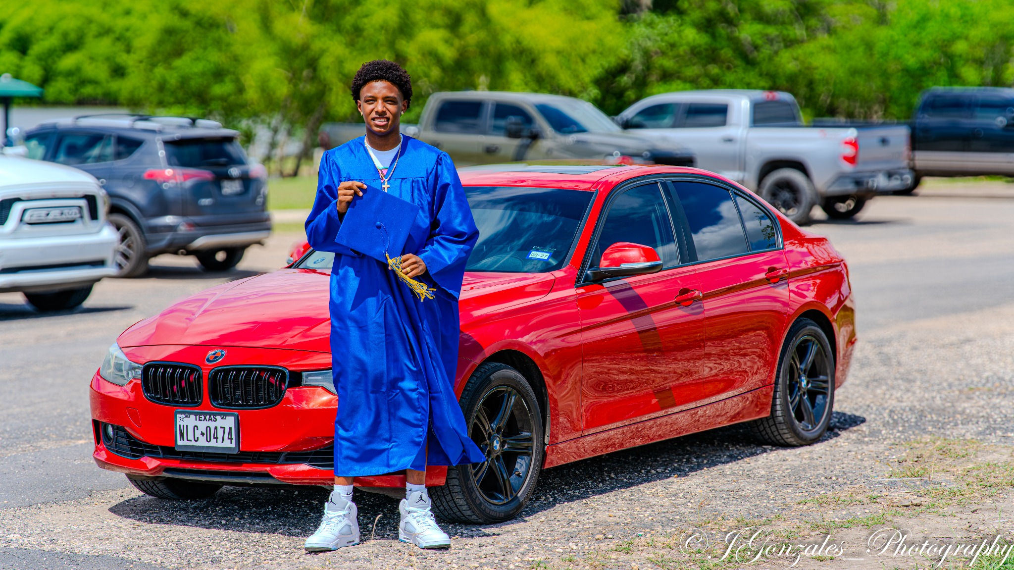 Graduate in cap and gown standing beside a red car