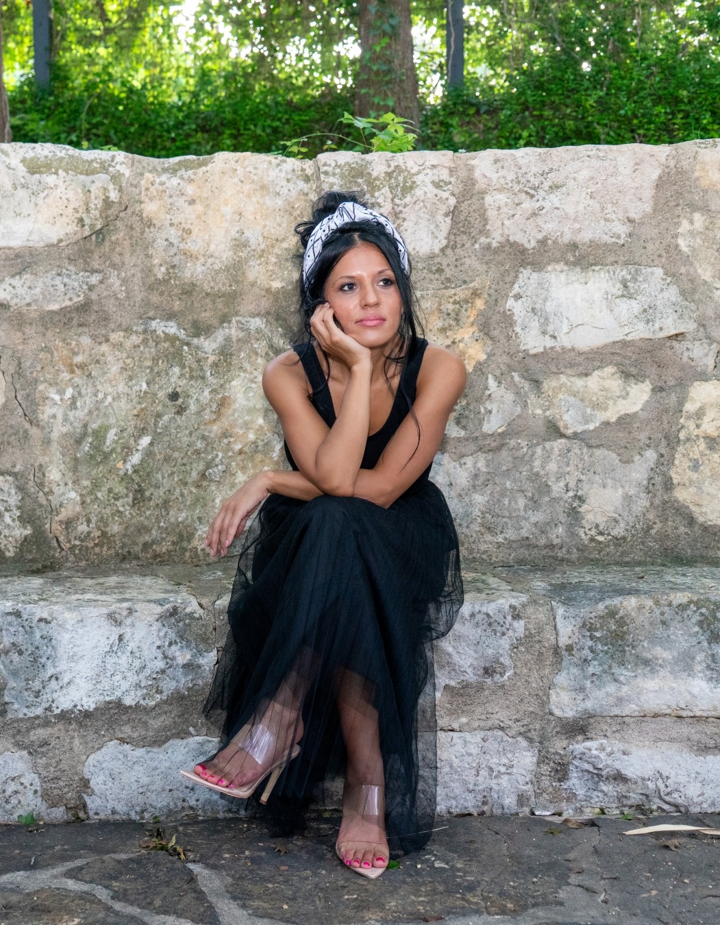 Woman in a black dress seated against a stone wall